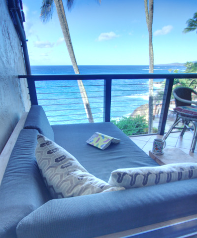 Day bed with view of ocean and palm trees. Book on bed and coffee cup next to bed.